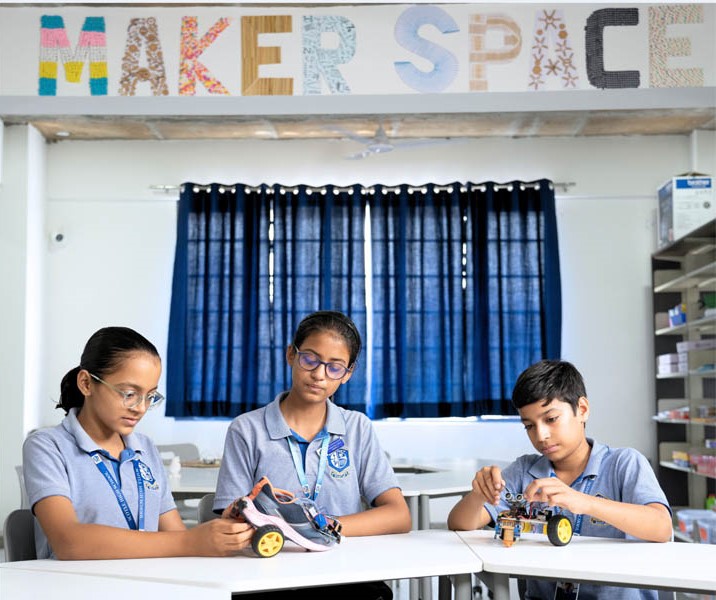 Three students in school uniforms work on robotics projects in a well-lit classroom labeled "Maker Space," seamlessly blending science and technology.