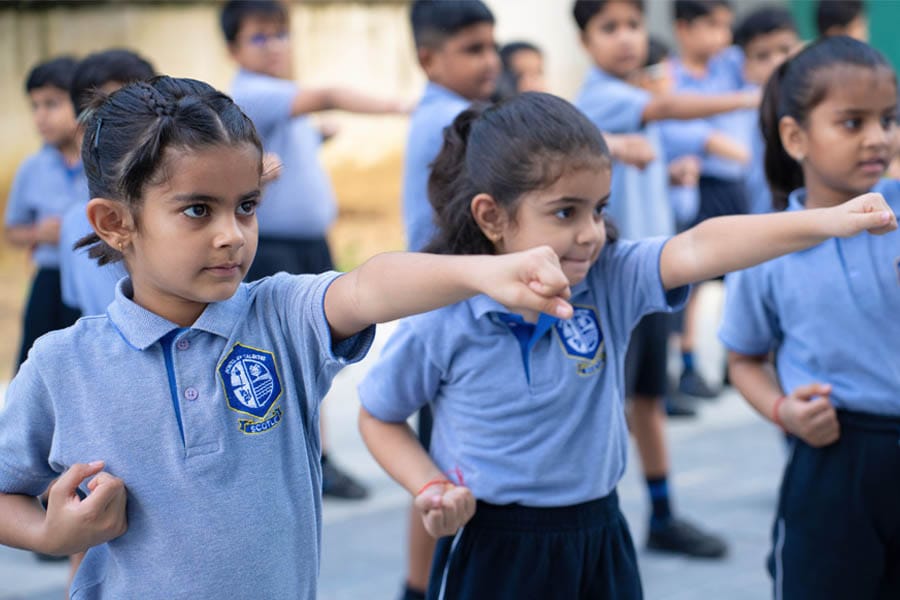 Children in blue martial arts uniforms practice in an outdoor area, performing punches with focused expressions.