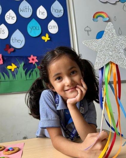 A young girl sitting at a table with a rainbow craft in the best kindergarten school in Jaipur.