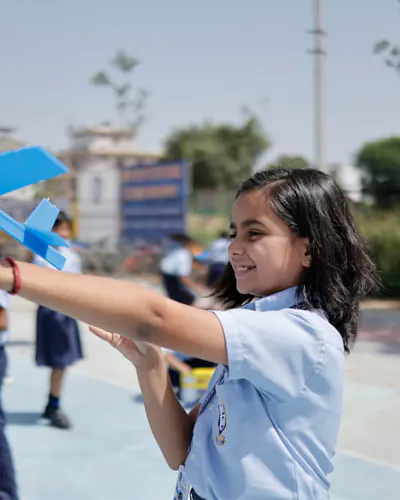 A girl in the best CBSE school uniform holding a toy airplane.