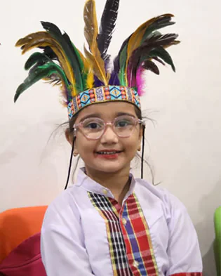 A little girl wearing a feather headdress from arts & craft at Scotle High School and glasses.