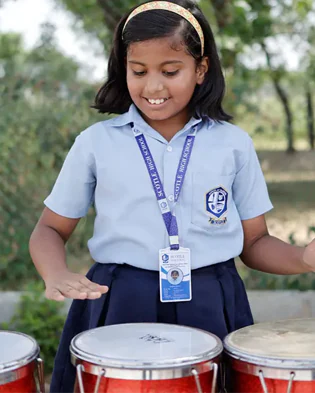 A girl in school uniform playing a conga drum.